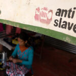 Woman using sewing machine below an Anti-Slavery International banner
